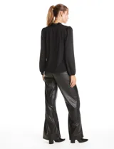 Blusa de seda fría color negro, con escote en V y lazo decorativo al cuello. Presenta mangas largas abullonadas con puños elásticos y detalles de strass aplicados en cuello, lazo y mangas.