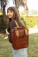 Matera mochila unisex de cuero marrón, con diseño estructurado, bolsillo frontal con cierre, asas superiores y correas ajustables.