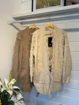 Sacón de punto color beige con flecos decorativos en los bordes y dos bolsillos delanteros.