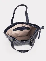 Cartera tote de cuero vacuno negro con acabado de aspecto envejecido. Cuenta con doble asa de hombro, costuras verticales decorativas, detalle de borla colgante con flecos y cierre superior.