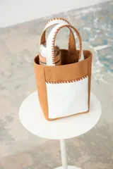 Matera de cuero color tostado con bolsillo frontal y asas en cuero blanco craquelado, con detalles de costuras bordadas a mano y espacio interior diseñado para termo y mate.