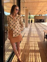 Camisa beige de muselina con estampado de lunares negros, cuello camisero, mangas largas con puños elásticos y cierre frontal con botones.
