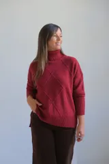 Polerón de cuello alto con diseño de rombos en relieve, mangas largas con puños acanalados y ruedo asimétrico con aberturas laterales.