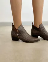 Botín corto color beige con textura símil piel de cocodrilo, taco de madera y laterales con corte en V.