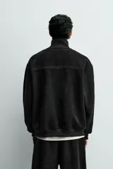 Sudadera de corte relajado confeccionada en pana con interior de tejido polar. Presenta cuello subido con cierre frontal de cremallera, manga larga y acabados en rib. Incluye bajo ajustable con cremalleras laterales.