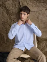 Camisa de corte clásico confeccionada en tejido Oxford de algodón, con diseño de rayas verticales finas en color celeste y blanco, cuello camisero, cierre frontal con botones y bolsillo en el pecho.