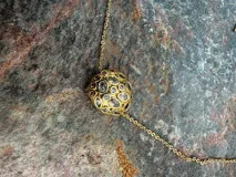 Collar de cadena fina dorada con dos dijes esféricos texturizados e incrustaciones de piedras de colores y zirconias.