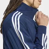Campera deportiva Adidas Originals Firebird Drop Needle de color azul marino, con cierre frontal, cuello alto y bolsillos laterales. Presenta las clásicas tres tiras blancas en las mangas, el logotipo del Trifolio bordado en el pecho y un sutil patrón de rayas verticales en relieve.