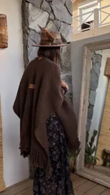 Ruana de lana merino color marrón chocolate, con textura tejida y terminación de flecos en el ruedo. Presenta un detalle de etiqueta de cuero en la parte superior de la espalda.