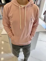Canguro de felpa color rosado, con capucha ajustable mediante cordones blancos, bolsillo tipo canguro frontal y pequeño logo bordado en el pecho.
