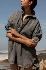 Vestido camisero corto de denim azul, con cuello camisero, cierre frontal con botones y mangas largas con puños abotonados.