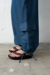 Pantalón estilo babucha color azul, de corte ancho con pretina ancha fruncida y cordones cruzados al frente. Cuenta con bolsillos cargo laterales y botamangas ajustables.
