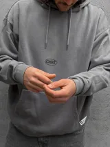 Canguro con capucha gris de corte holgado, con bolsillo frontal tipo canguro y logo pequeño estampado en el centro del pecho.