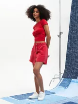 Short pollera de denim color rojo con diseño cruzado, cierre frontal de botones metálicos y acabado desmechado en el ruedo.