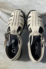 Sandalias de cuero color crema, con diseño de tiras entretejidas y hebilla ajustable en el tobillo.