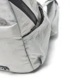 Mochila de nylon color gris, con cierre superior, bolsillo frontal con cierre, bolsillos laterales, manija superior de mano y aplique de cuero sintético con logo grabado en la parte inferior.