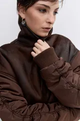 Cazadora de estilo bomber con diseño híbrido, combinando paneles de tela técnica en las mangas con un cuerpo de efecto piel desgastada y forro interior de corderito sintético. Presenta cierre frontal, cuello amplio y puños elásticos.