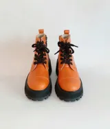 Borcego de cuero color naranja de caña media, con suela de plataforma y taco grueso negro, cordones oscuros y cierre lateral.
