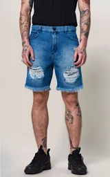 Bermuda de denim azul con efecto desgastado y roturas en ambas piernas. Presenta bordes deshilachados y un forro estampado visible en las aberturas. Tiene cierre frontal con botón metálico y cinco bolsillos.