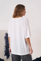 Remera blanca de manga corta con silueta amplia y cuello redondo. Presenta una estampa frontal que simula una camisa con corbata en tonos grises.