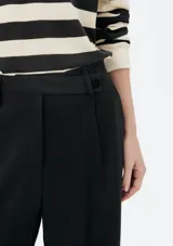 Pantalón de vestir de corte recto y tiro alto, con cierre frontal y trabillas para cinturón. Presenta pinzas en la parte delantera que aportan estructura a la prenda.