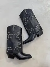 Botas texanas de caña media, color negro, con diseño de ojales metálicos plateados distribuidos en la caña. Presentan taco cuadrado y punta ligeramente cuadrada.