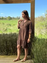 Vestido corto de lino color beige claro, con cuello mao, escote con botones de nácar, mangas tres cuartos con volados y ruedo con volado.