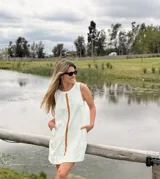 Vestido corto de jean crudo, de silueta holgada y sin mangas, con una tira vertical central de cuero color camel y bolsillos laterales.