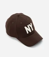 Gorra de béisbol de seis paneles, color marrón oscuro, con ala curva y bordado frontal de las letras "NY" en blanco. Posee cierre ajustable tipo strapback.