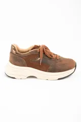 Zapatilla urbana de cuero lavado en tonos marrones, con paneles de gamuza y detalles metalizados en el talón. Presenta cordones al tono y una suela de plataforma de goma en color crema.