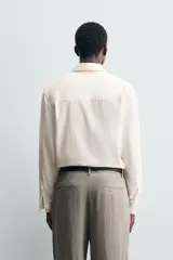 Camisa de hombre de corte relajado (relaxed fit) en tejido de mezcla de algodón y viscosa, color beige claro con finas rayas verticales. Presenta cuello italiano y manga larga con puño abotonado.