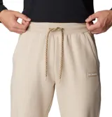 Pantalón de jogging color beige, confeccionado en mezcla de algodón, con cintura elástica ajustable mediante cordón, bolsillos laterales y bolsillo trasero. Presenta puños acanalados en los tobillos y un pequeño parche con el logo de la marca en la parte frontal.