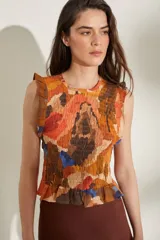 Top sin mangas con diseño fruncido tipo smock y estampado abstracto en tonos naranjas, marrones y azules. Cuenta con cuello redondo y pequeños volados en las sisas y en el ruedo.