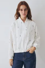 Campera tipo bomber de lino y algodón, con cierre frontal y puños elásticos. Presenta un estampado integral con motivos deportivos sobre fondo blanco.