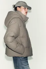 Campera puffer corta de tejido engomado resistente al viento, con aislamiento térmico. Presenta cuello subido con capucha, manga larga, bolsillos delanteros y bajo ajustable con stoppers laterales. Cierre frontal con cremallera termosellada y botones magnéticos.