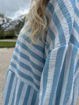 Camisa oversize celeste con rayas verticales blancas, de manga larga y cuello clásico.