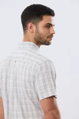 Camisa de manga corta confeccionada en mezcla de lino y algodón, con diseño a cuadros en tonos gris, blanco y azul. Presenta cuello camisero con botones y bolsillo ojal en el pecho con detalle bordado.