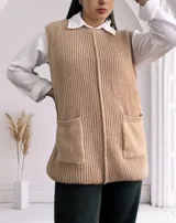 Chaleco largo de punto color beige, con cuello redondo y bolsillos frontales. Diseño sin mangas y corte recto.