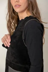 Chaleco de cuero negro con diseño sin mangas, corte recto y bolsillos frontales con contraste de textura. Presenta costuras visibles y un acabado artesanal.