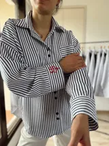 Camisa oversize a rayas verticales blancas y negras con bordado rojo en el frente.