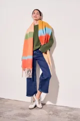 Bufanda larga tejida a rayas horizontales en tonos naranja, celeste, amarillo y beige, con flecos en los extremos.