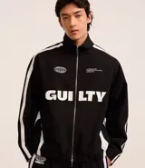 Campera deportiva negra con cuello alto y cierre frontal. Presenta franjas blancas contrastantes a lo largo de las mangas y detalles gráficos en blanco en el pecho, incluyendo la palabra "GUILTY" en grande.