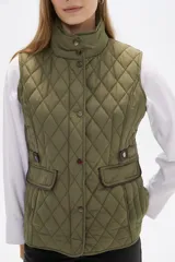Chaleco acolchado de diseño capitoneado en color verde militar, con cuello alto, cierre frontal con botones a presión y bolsillos laterales con solapa y detalles en contraste.
