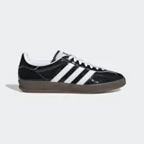 Championes Adidas Gazelle Indoor negros de cuero charol, con las tres tiras laterales blancas y suela de goma marrón.