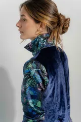 Camisa de seda con cuello clásico y cierre frontal de botones, de manga larga con puños abotonados. Presenta un estampado floral en tonos azules, verdes y rosados sobre fondo negro.