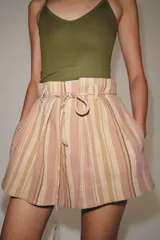 Bermuda de tiro medio con diseño de rayas verticales en tonos rosados y beige. Presenta cintura con trabillas, cinturón ajustable con lazada, bolsillos laterales y detalle de pliegues en el delantero.