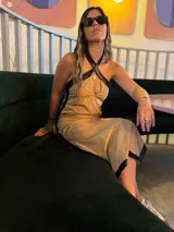 Vestido midi color arena con detalles en cuero negro en el escote, sisas y ruedo. Presenta escote halter cruzado y corte recto.