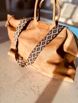 Bolso grande tipo tote de cuero color marrón gastado, con doble asa corta de madera y correa larga de tela estampada.