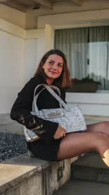 Tote bag de diseño rectangular con acabado texturizado en tono grisáceo con efecto jaspeado. Presenta doble asa superior y cierre frontal metálico tipo torniquete en color dorado.