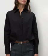 Camisa básica de mujer confeccionada en tricolina de algodón, con cuello solapa, cierre frontal de botones y mangas largas con puños abotonados.